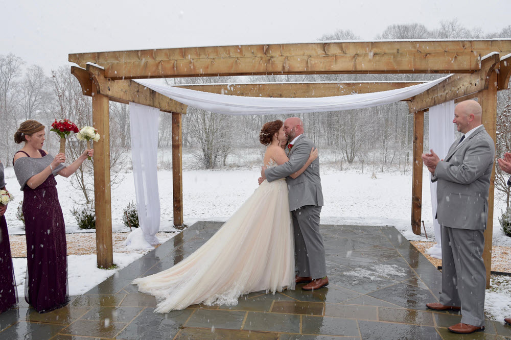 Bridal couple celebrating their winter wedding amidst falling snow.