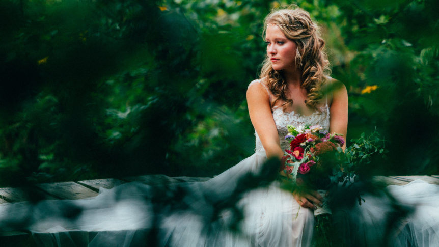 Bride elegantly seated on a bridge, holding a vibrant bouquet of flowers.