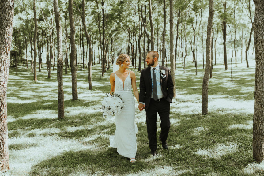 Bride and Groom Holding Hands While Strolling in a Sunlit Forest, Sharing a Loving Gaze