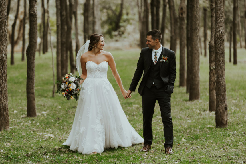 Bridal Couple Walking Hand in Hand in Walnut Grove, Featuring Wedding Dress, Veil, and Bouquet