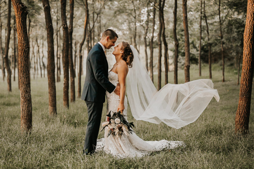 Wedding Couple in Forest with Flowing Veil and Beautiful Bouquet