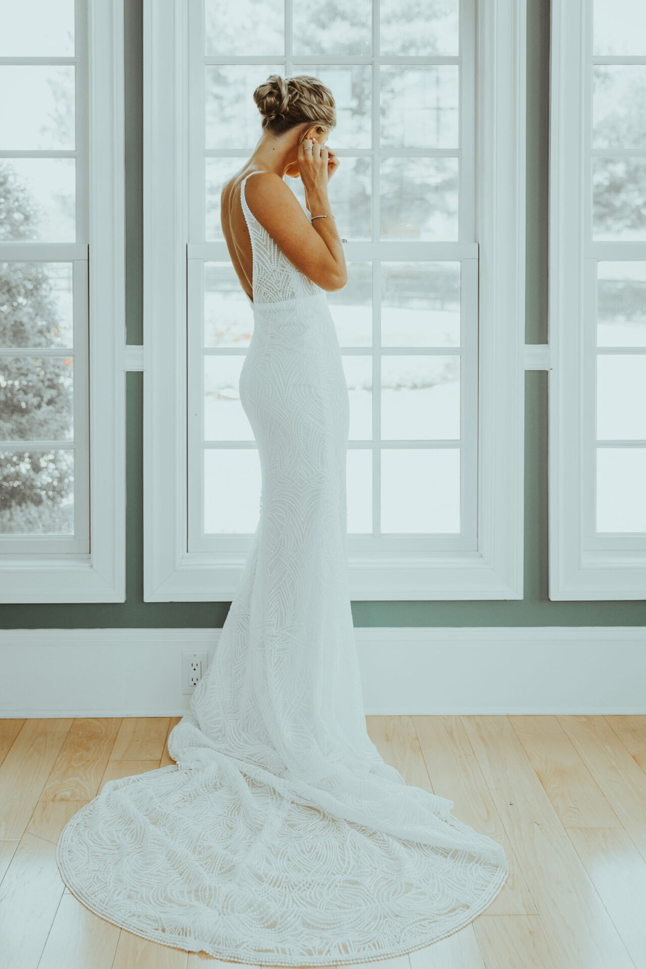 Zion Springs Real Wedding bride standing in front of white window in wedding dress fixing her earring