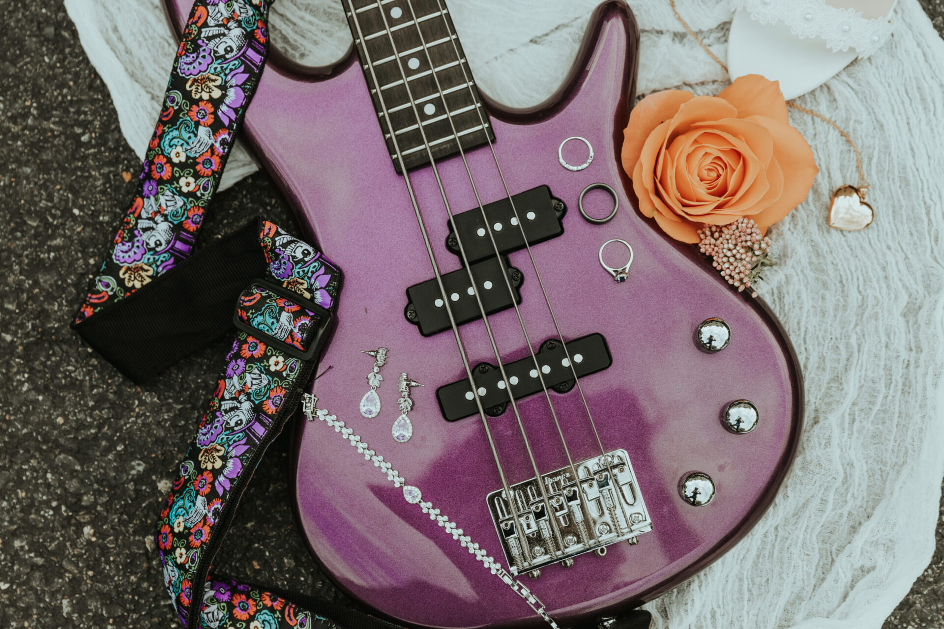 guitar with wedding rings, bride's necklace, bracelet and earrings with orange rose