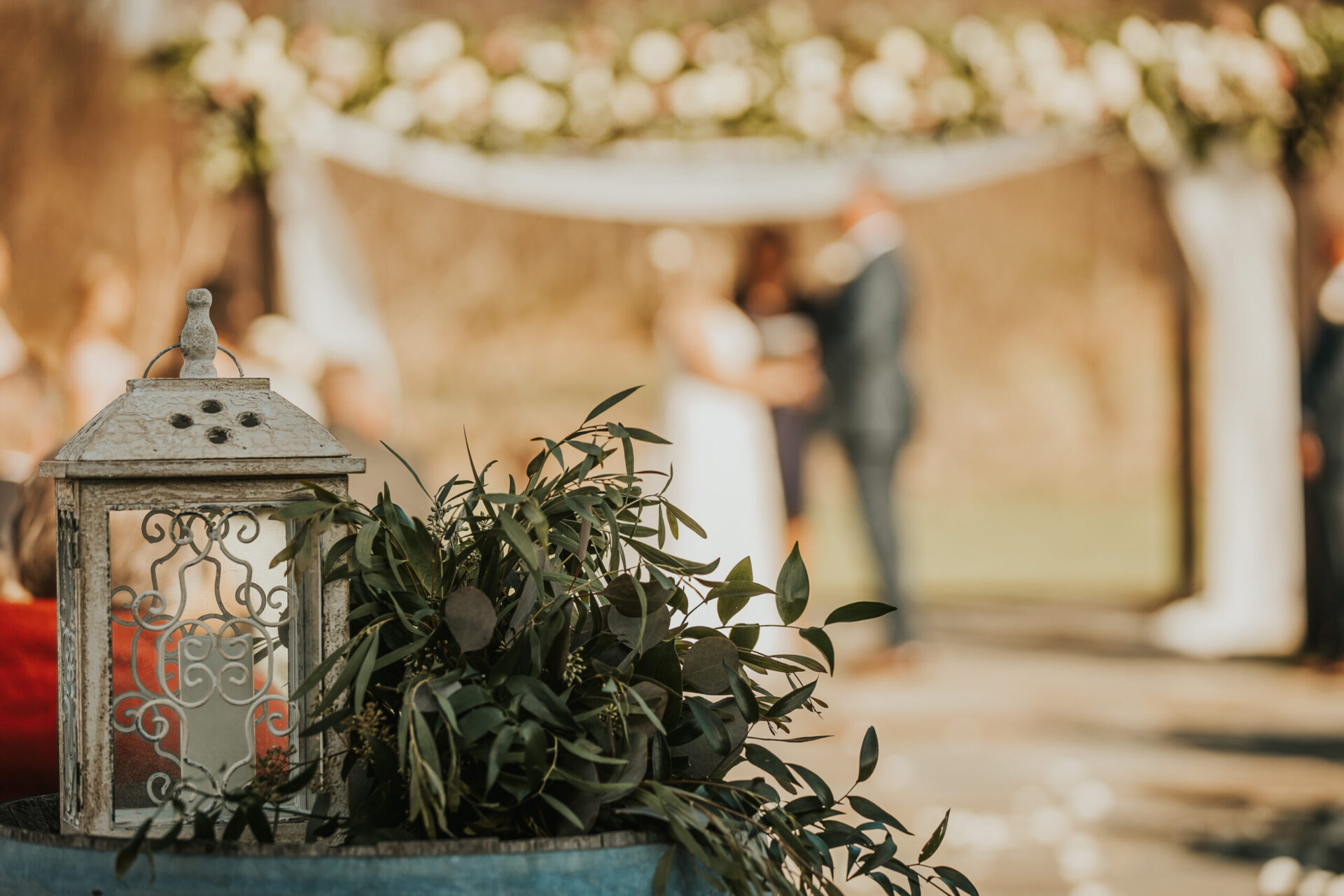 Zion Springs wedding ceremony white lantern with green foliage on rustic barrel white pergola