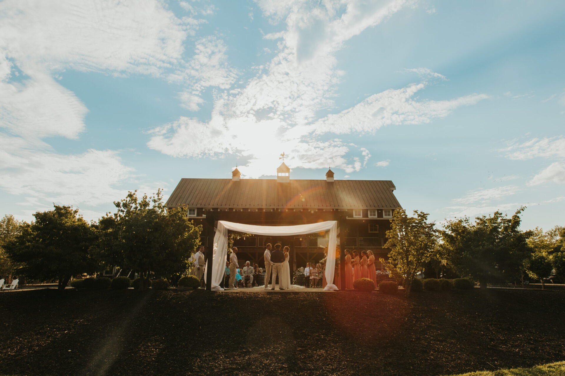 Zion Springs wedding ceremony under the pergola with the rustic barn as a sunlit background