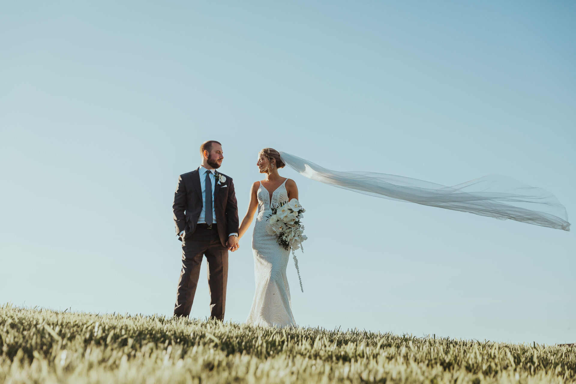 Zion Springs Real Wedding bride and groom on a hilltop with cloudless blue sky and veil floating in the breeze