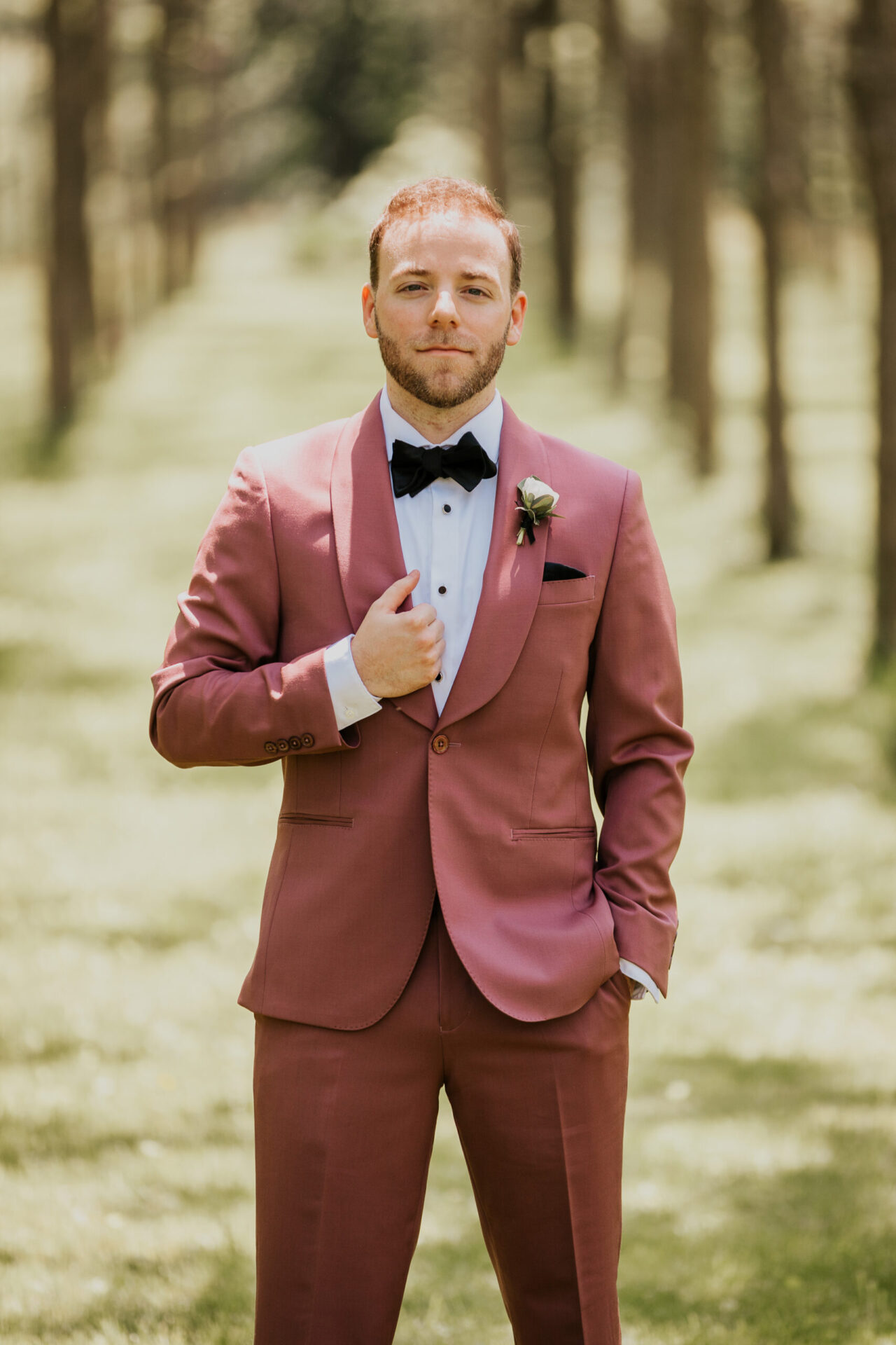 Zion Springs groom in dusky rose suit with black bow tie standing in walnut grove
