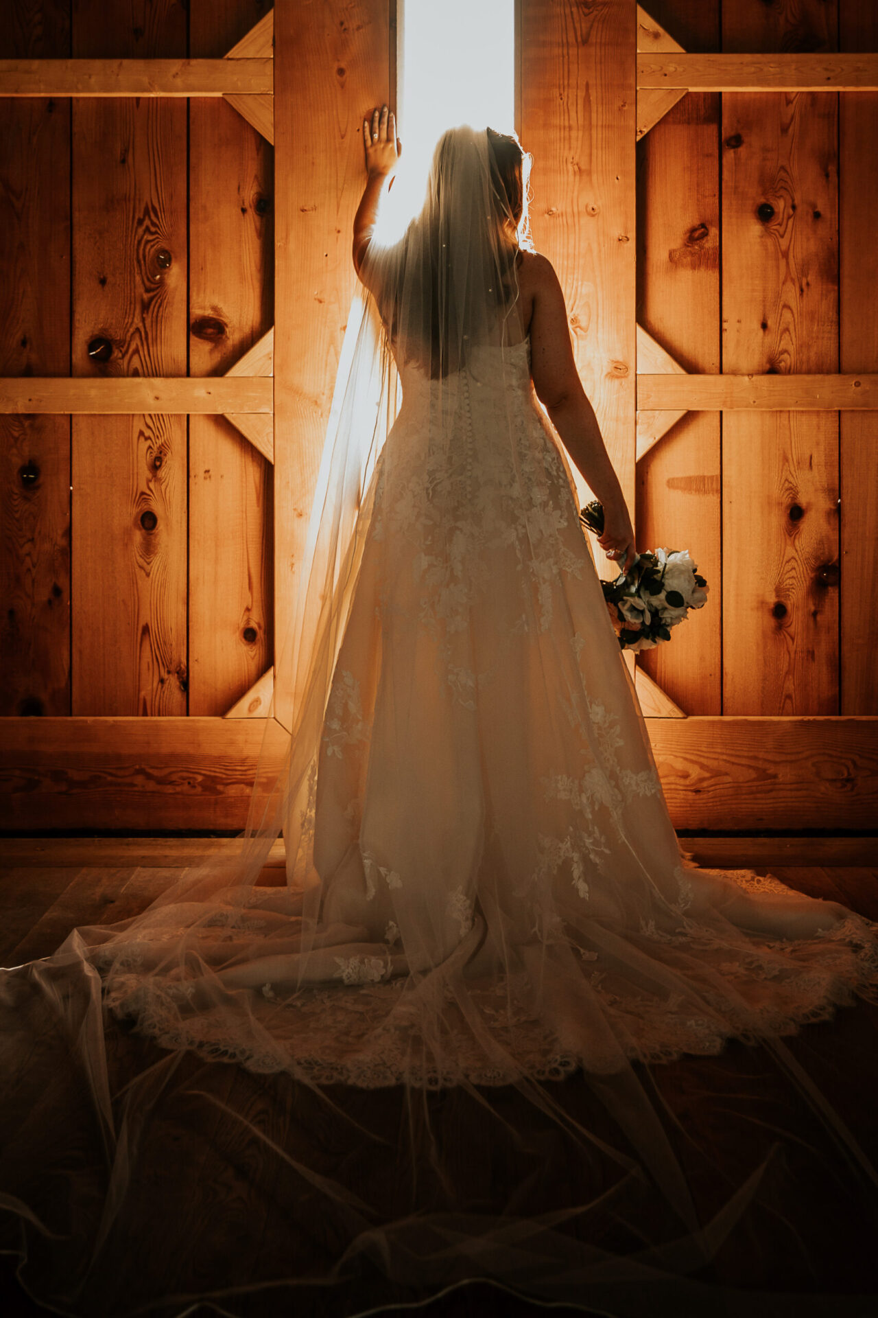 Zion Springs bride standing by the wood doors of rustic barn with backlit sunlight