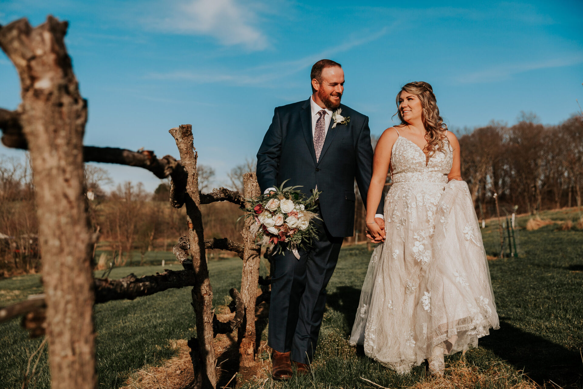 Zion Springs bride and groom strolling past rustic wood fence