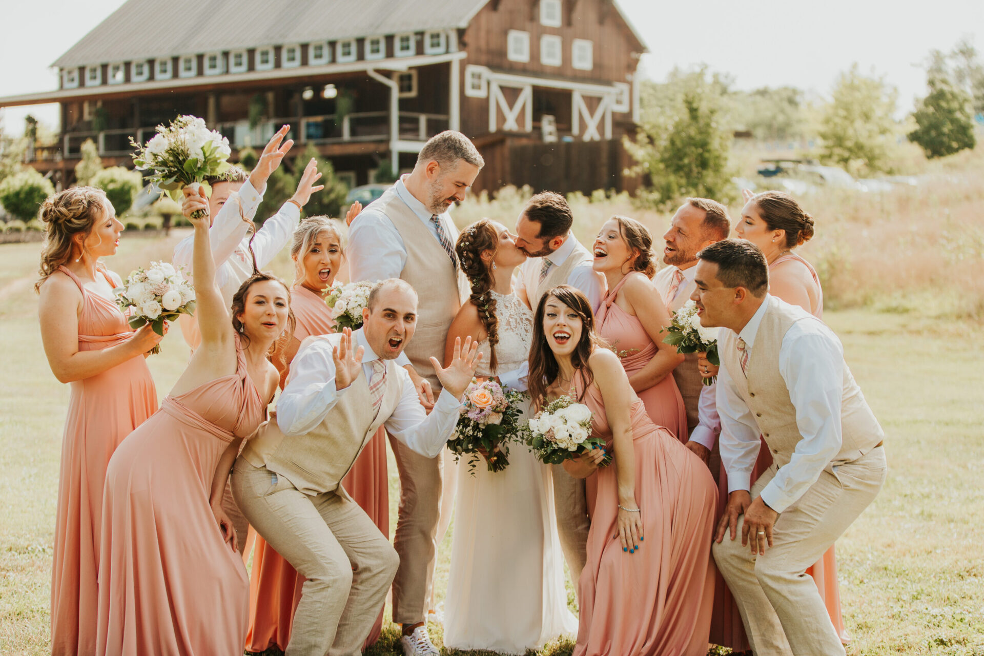 bride and groom embracing and surrounded by bridesmaids and groomsmen in front of Zion Springs rustic barn