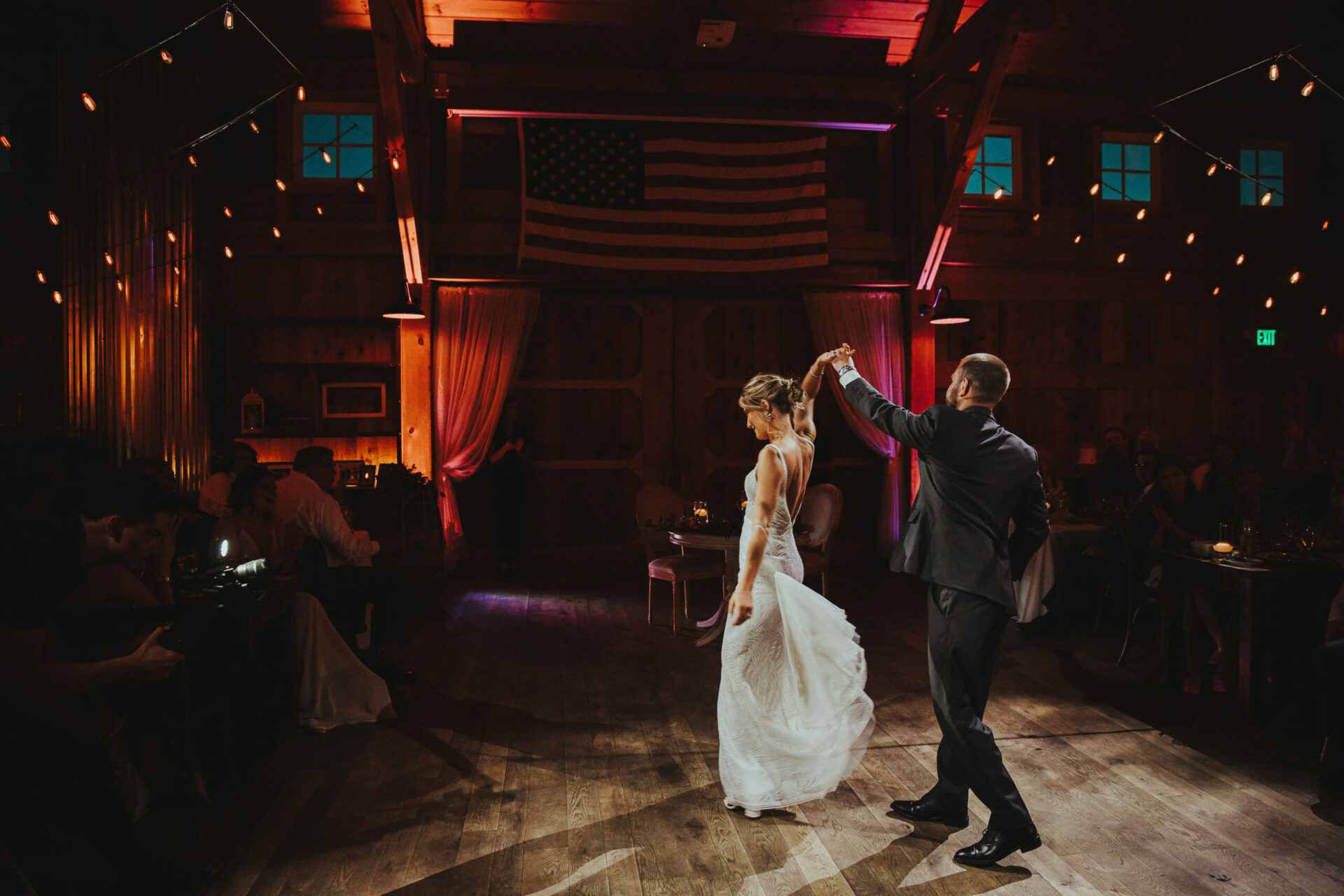 Zion Springs bride and groom dancing in rustic barn with spotlight and American Flag