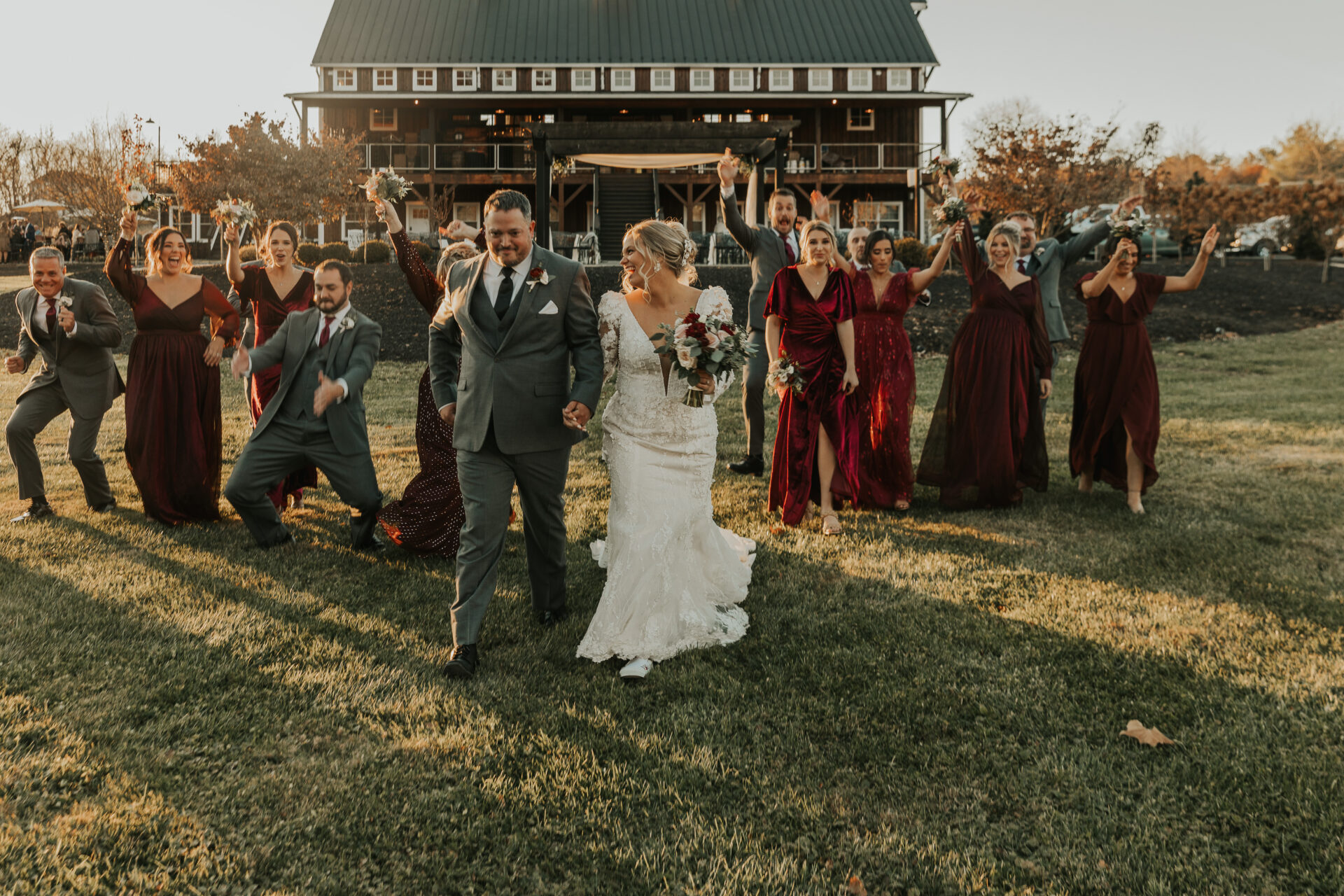 bride and groom celebrating with bridesmaids and groomsmen on field in front of rustic wedding venue