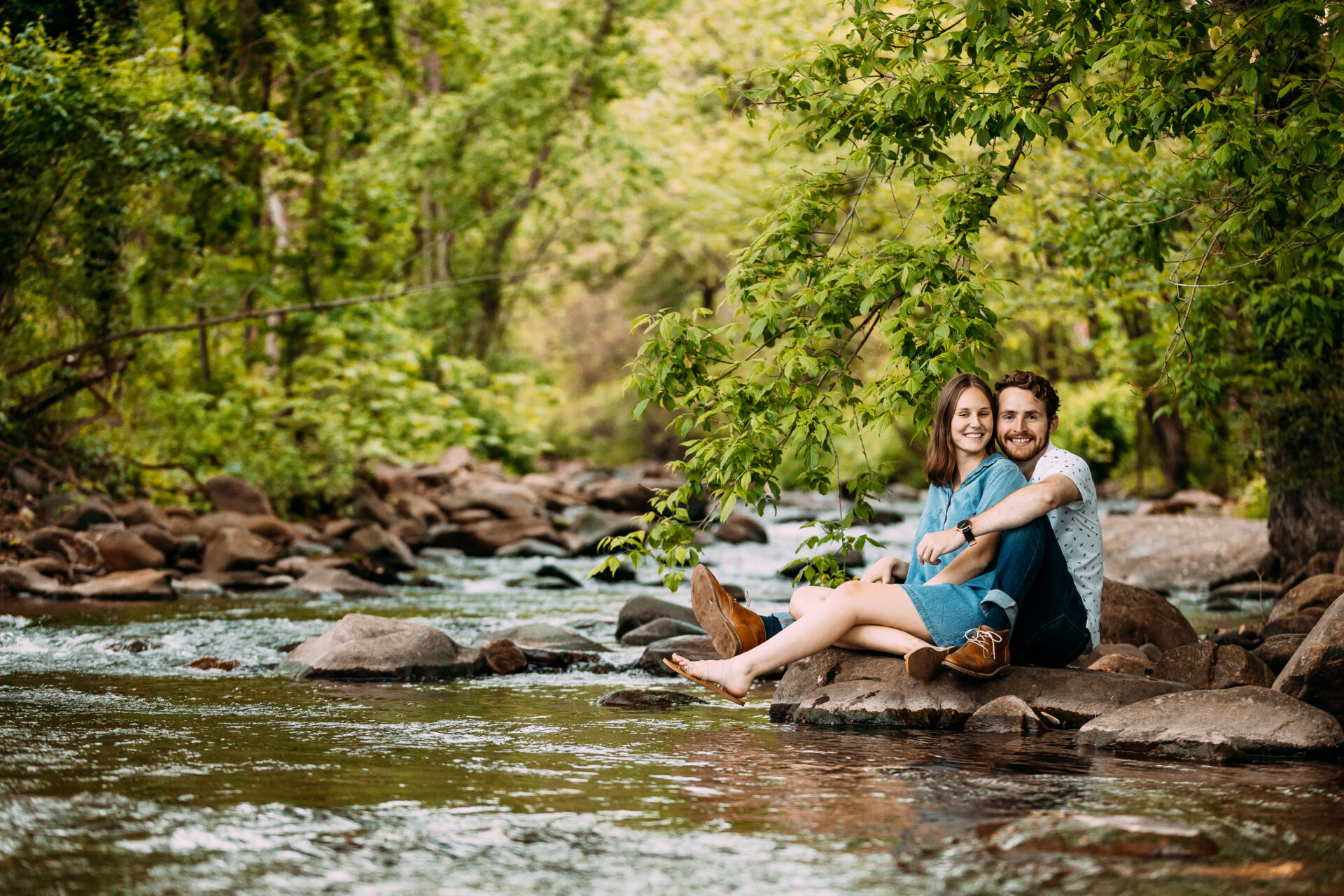 newly engaged couple sitting on rocks next to a creek